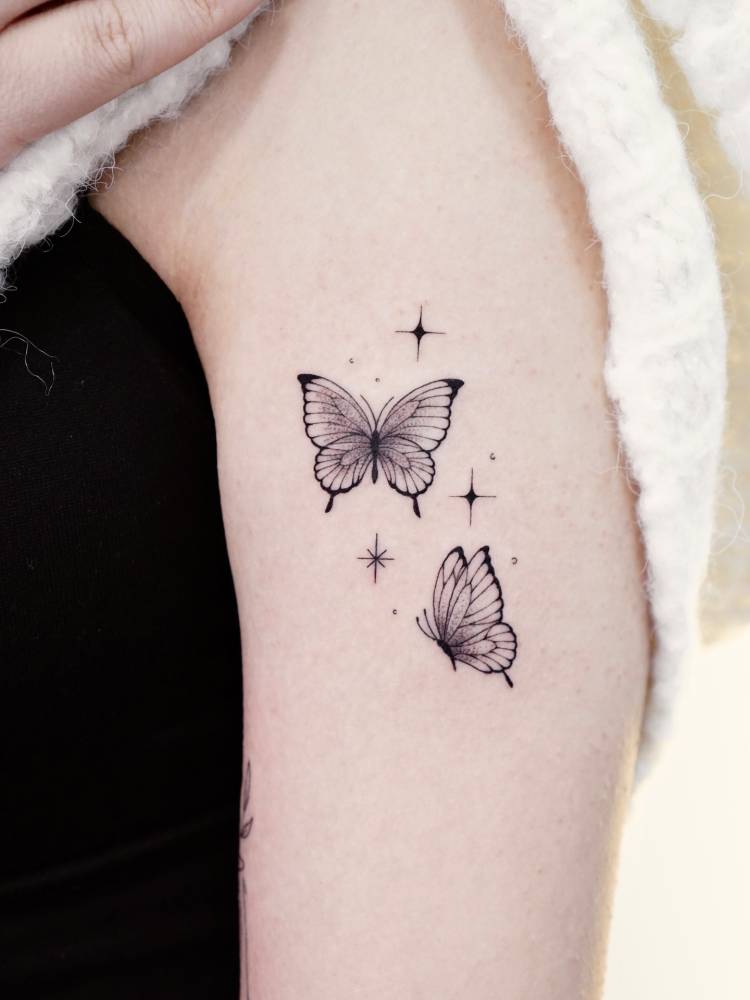 Illustrative style butterfly couple tattoo located on the upper arm.
