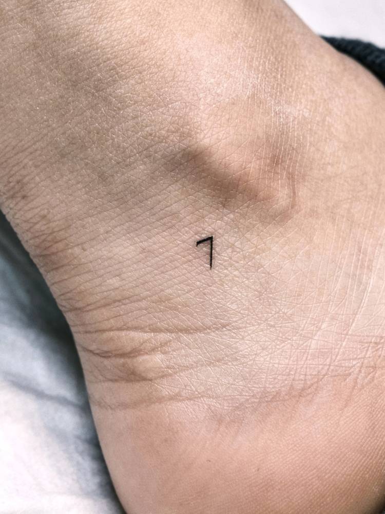 Minimalistic tattoo of the number "7" located on the ankle.