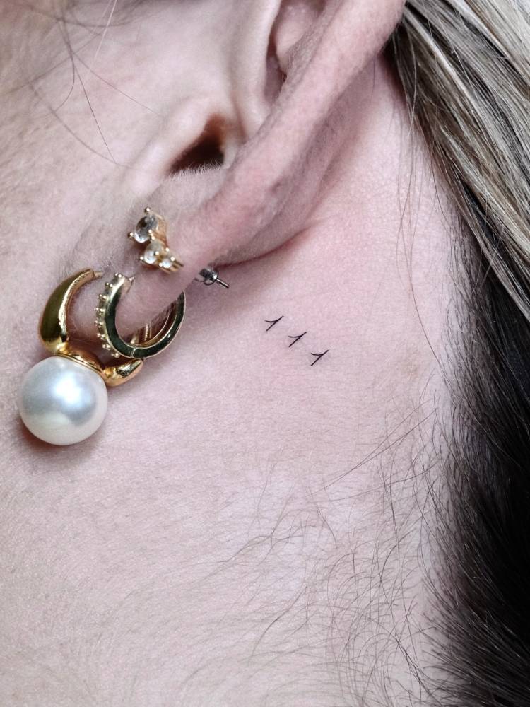 Angel number "111" tattoo placed behind the ear.