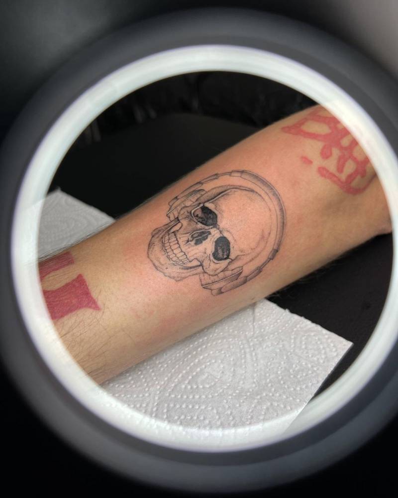Micro-realistic skull and headphones tattoo located on the forearm.