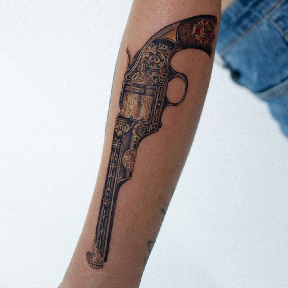 Micro-realistic style revolver tattooed on the forearm.