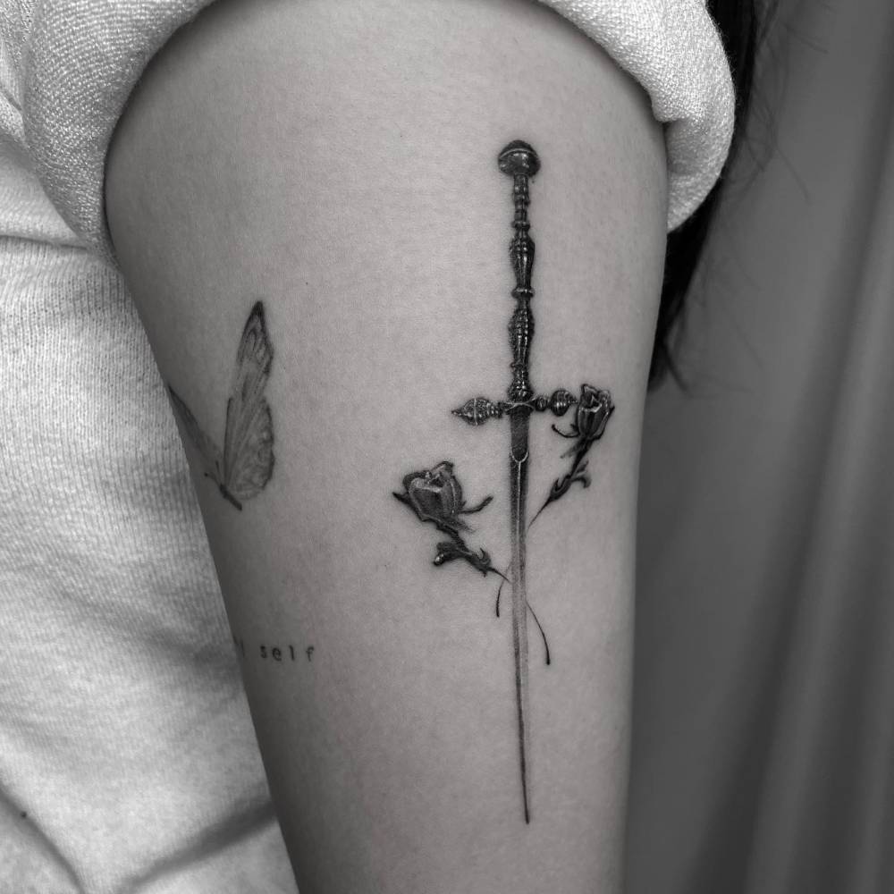 Blackwork style sword and roses tattoo located on the upper arm.