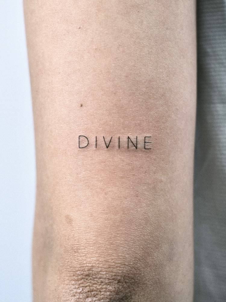 Sans serif font word "divine" tattooed on the tricep.