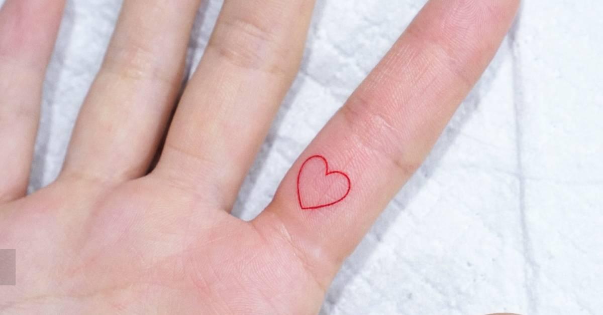 Tiny red heart tattooed on the finger, done in