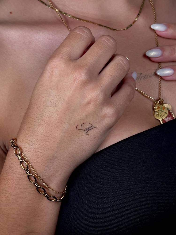 Script font letter "M" tattoo done on the hand.