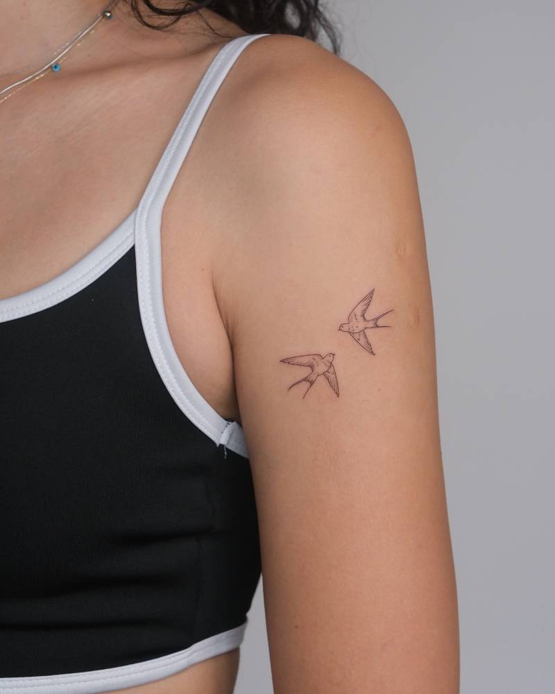 Flying swallows tattoo in fine line style located on the upper arm.