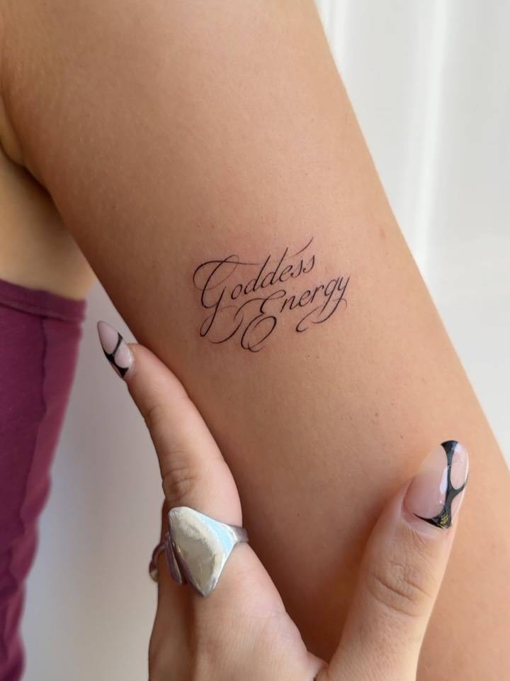"Goddess energy" lettering tattoo done on the upper arm.