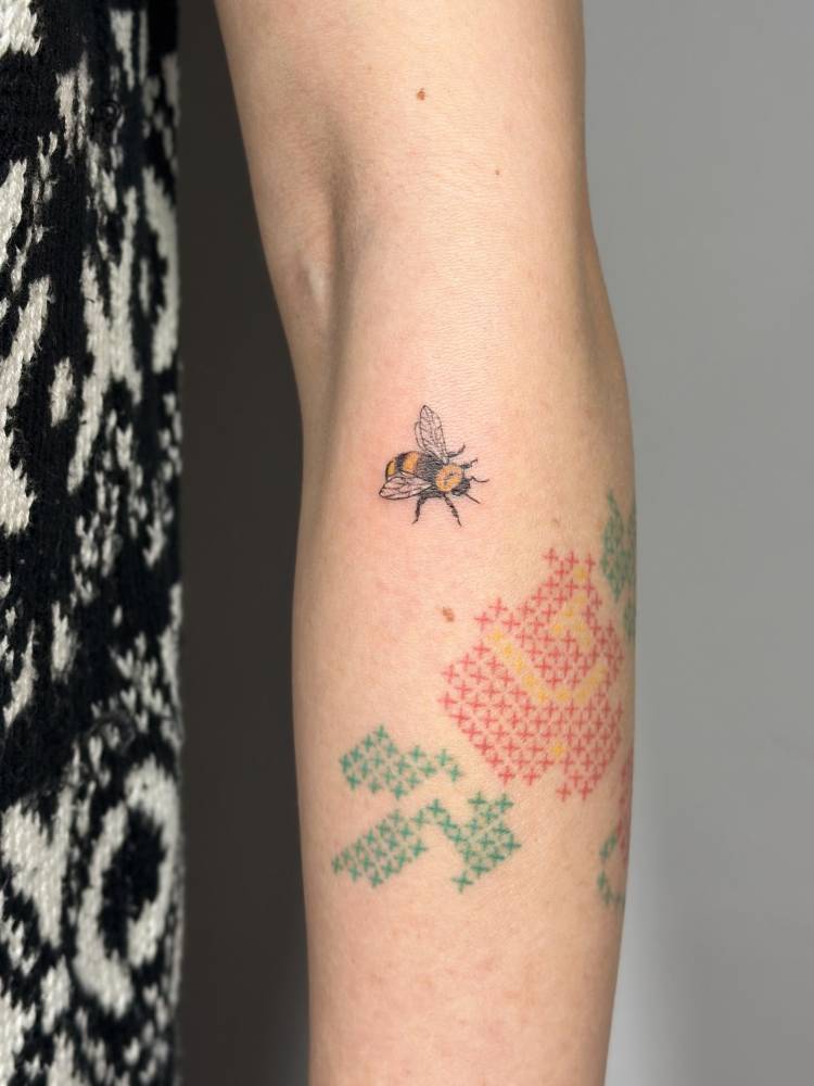 Little bee tattoo located on the forearm, illustrative style.