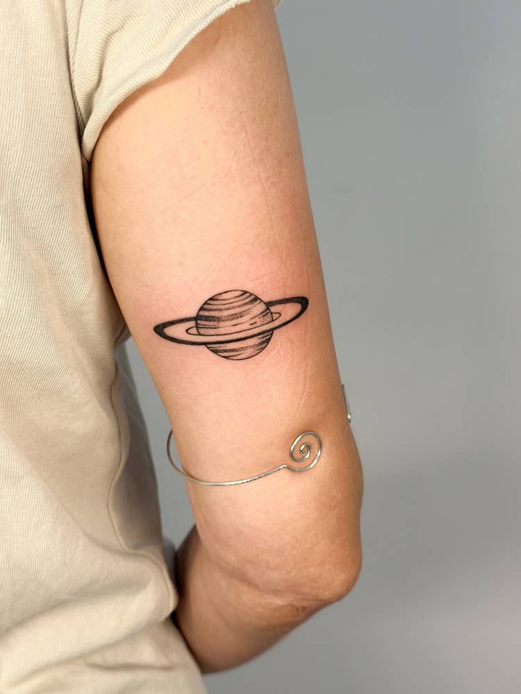 Saturn tattoo in illustrative style located on the tricep.