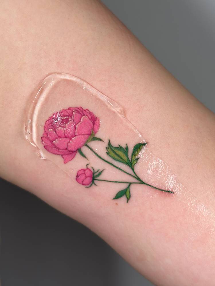 Pink peony tattoo in illustrative style located on the inner arm.