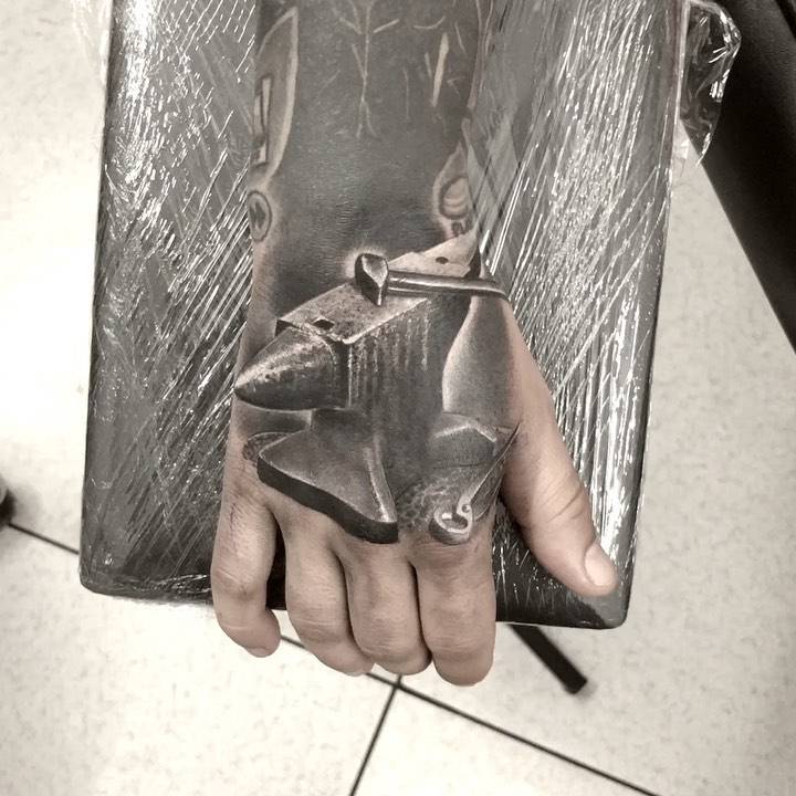 Black and grey anvil tattoo on the hand.