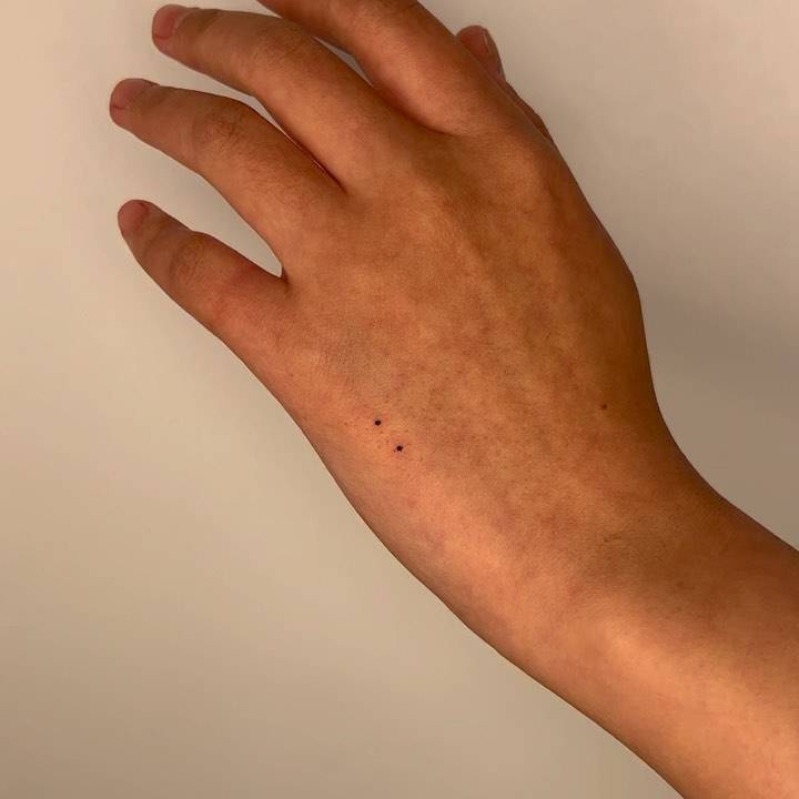 Two dots tattooed on the hand, minimalistic sytle.