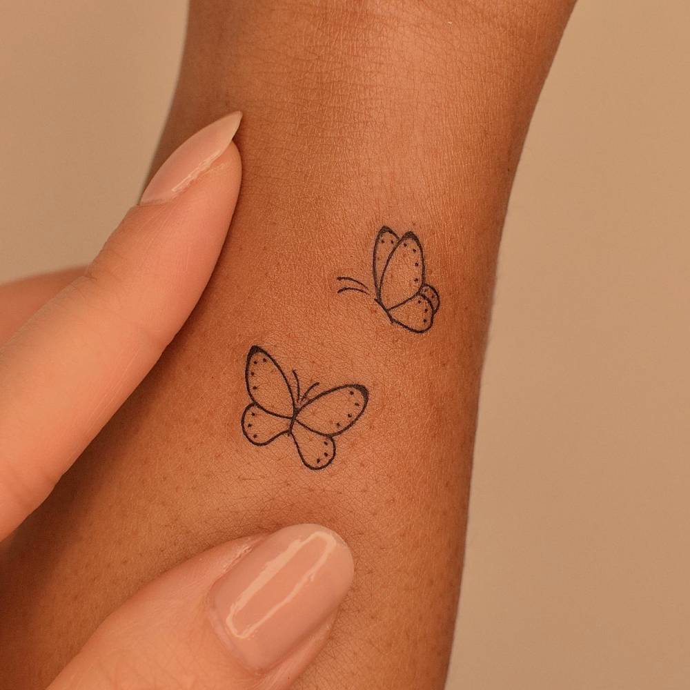 Minimalistic style butterfly couple tattoo located on the wrist.