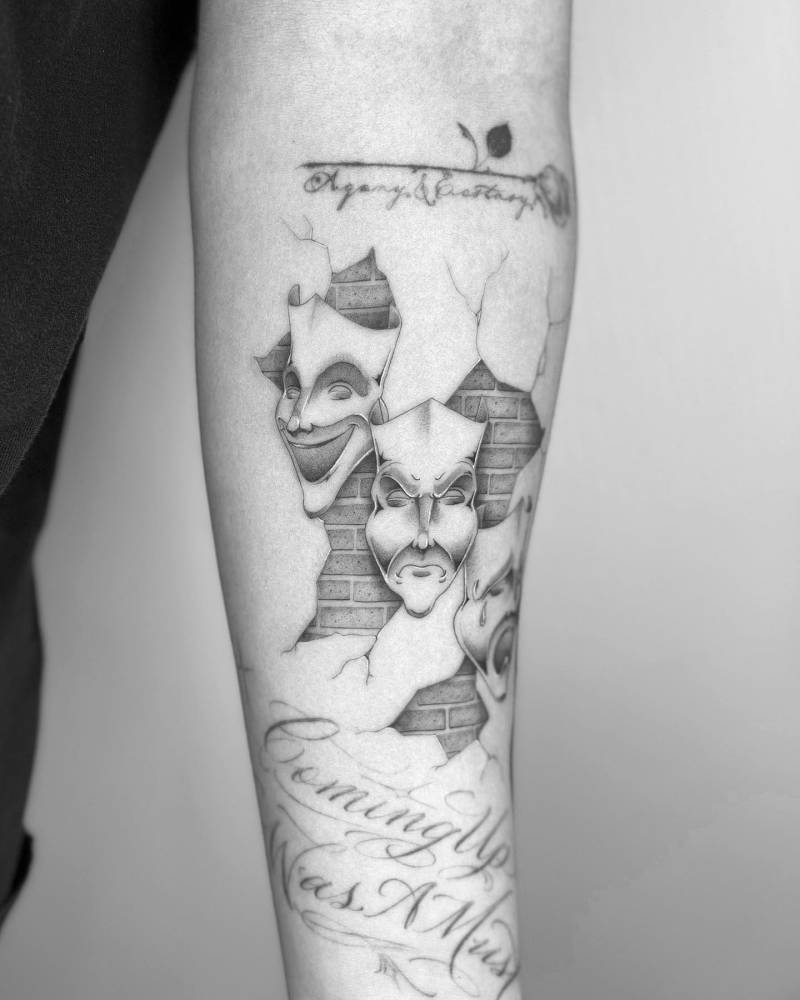 Single needle drama masks tattoo located on the inner forearm.