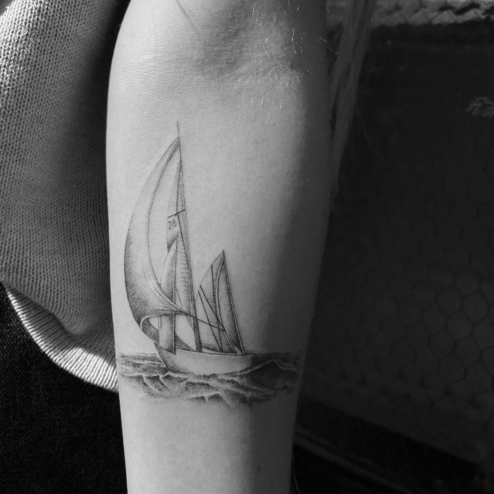 Micro-realistic style sailboat tattoo located on the inner forearm.