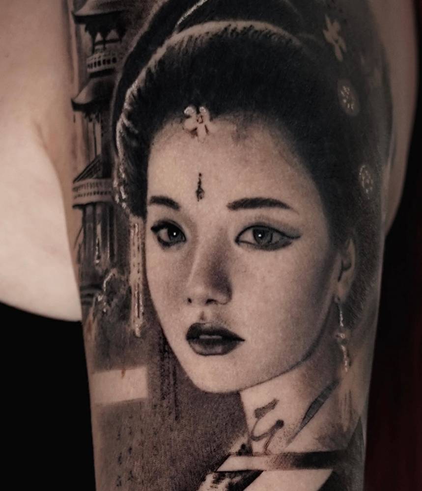 Geisha portrait tattoo located on the upper arm, black and grey style.