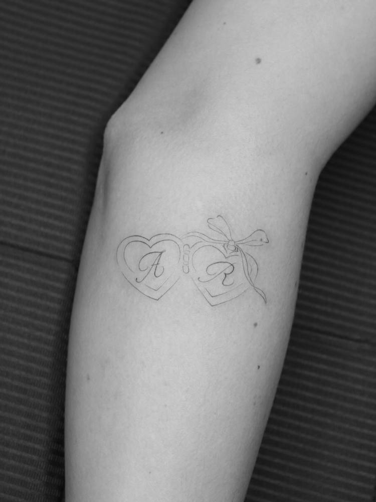 Heart pendants and initials tattooed on the inner forearm.