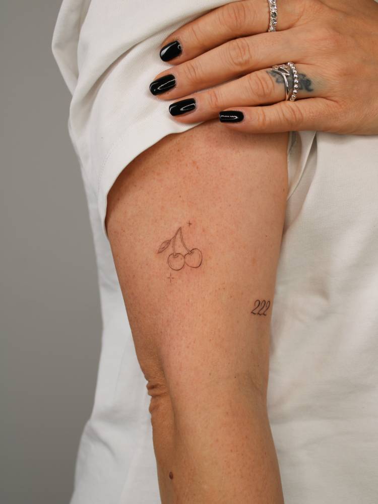 Cherries tattoo in fine line style placed on the upper arm.