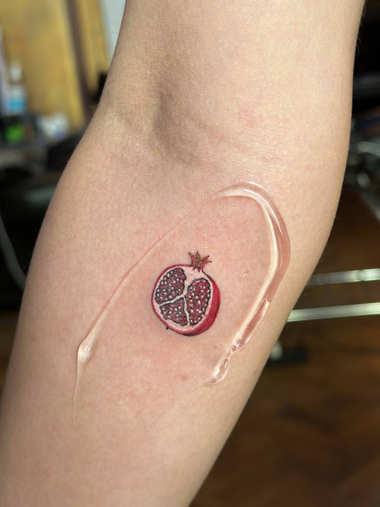 Little pomegranate in illustrative style located on the inner forearm.