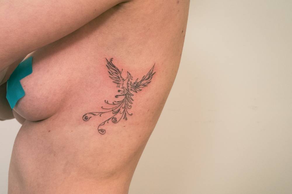 Phoenix tattoo in fine line style located on the side boob.