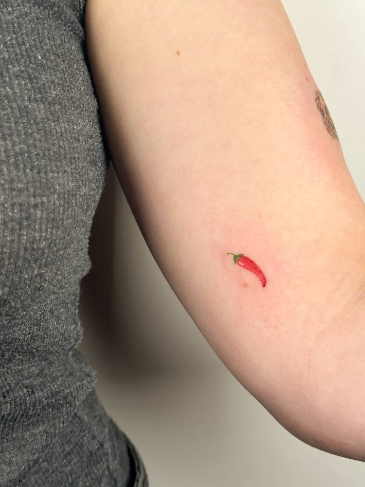 Tiny red chili tattoo located on the inner arm.