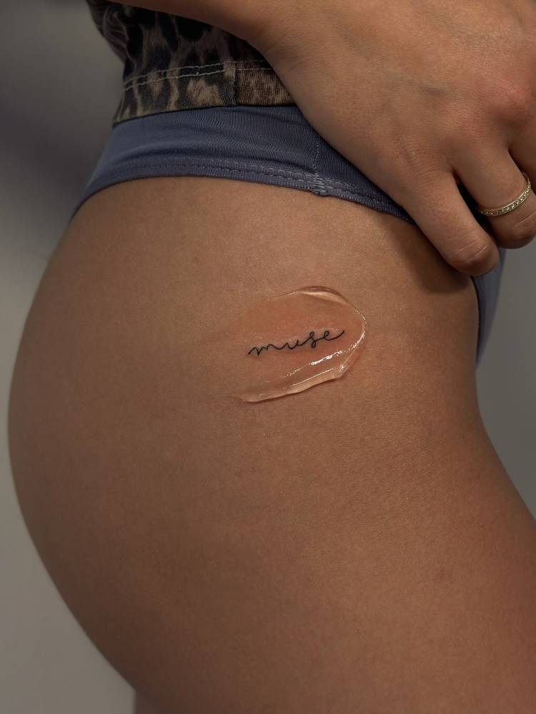 Handwritten font word "muse" tattooed on the hip.