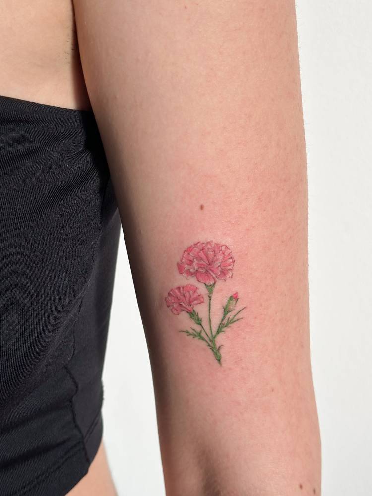 Carnation flowers tattooed on the upper arm, illustrative style.