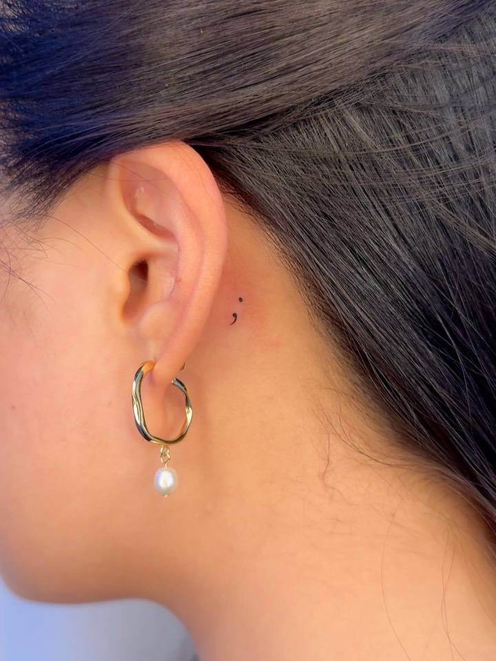 Tiny minimalistic semicolon tattoo done behind the ear.