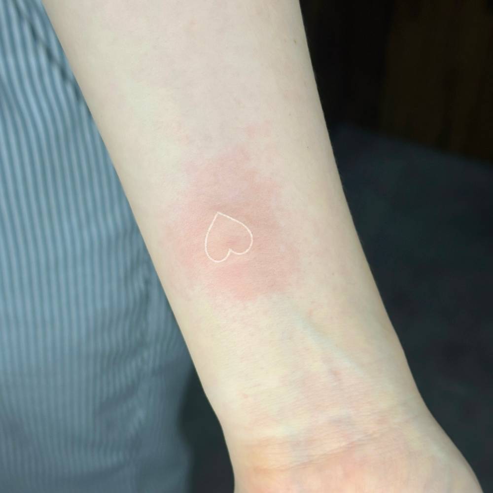 Minimalistic heart in white ink tattooed on the wrist.