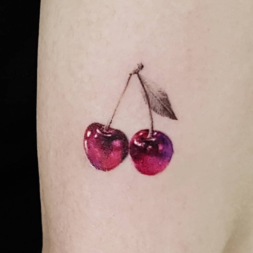Micro-realistic style cherries tattooed on the upper arm.