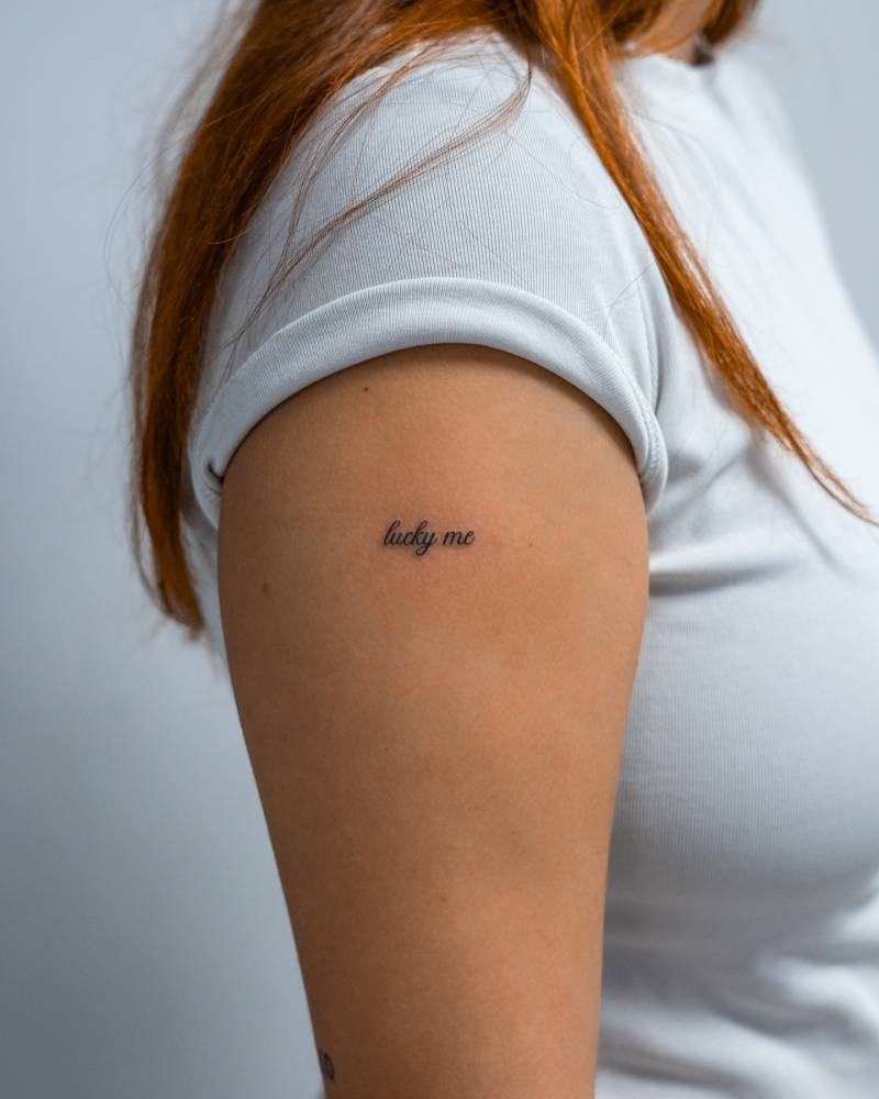 "Lucky me" lettering tattoo placed on the upper arm.