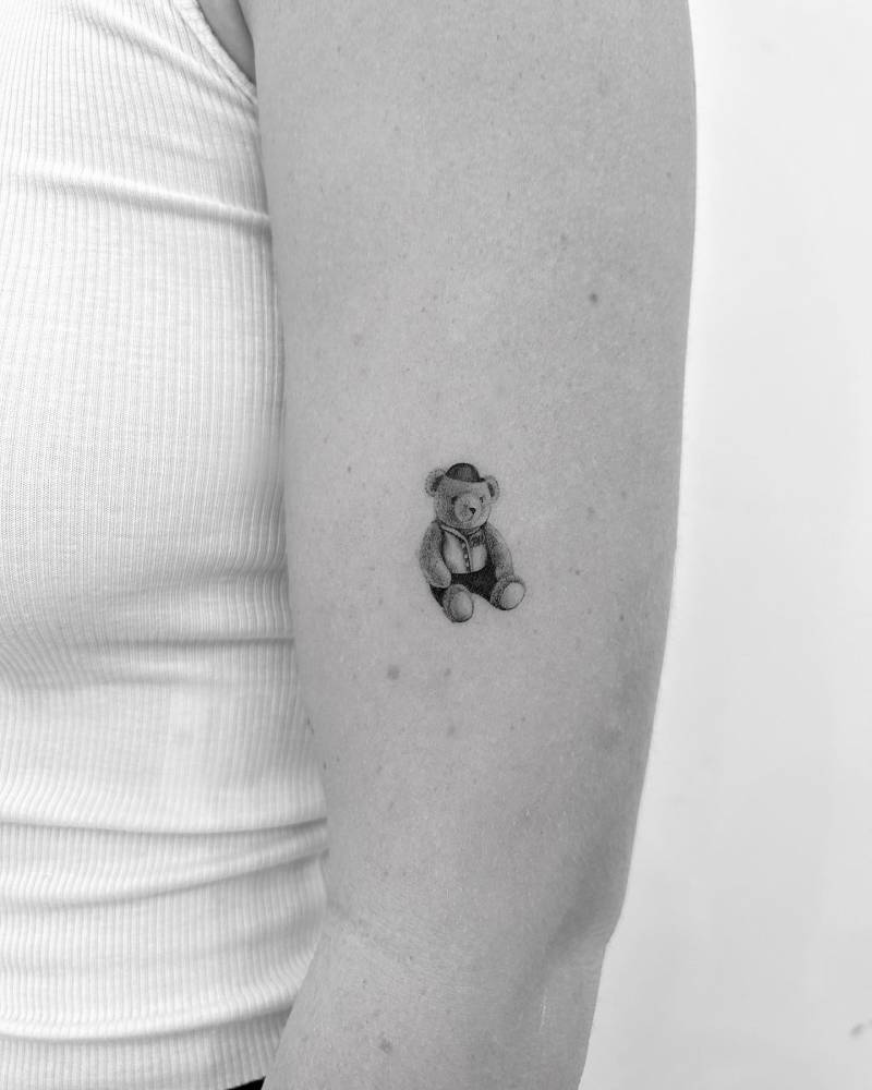 Micro-realistic style teddy bear tattoo located on the upper arm.