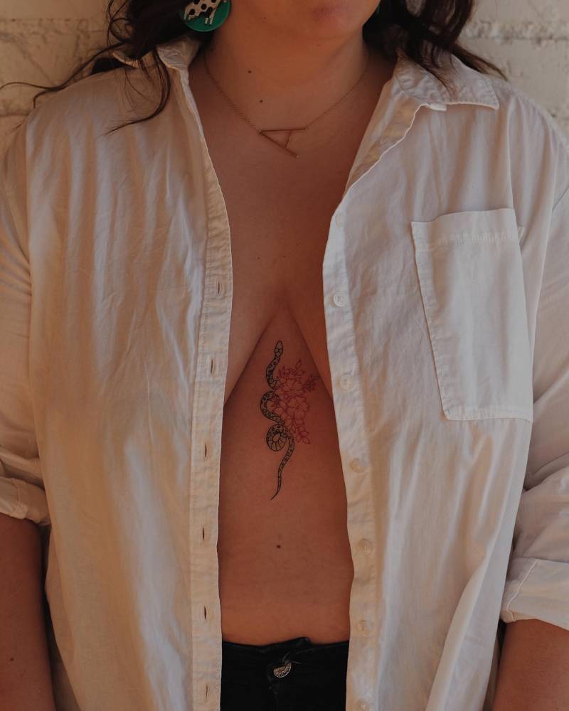 Fine line style snake and flower tattoo done on the sternum.