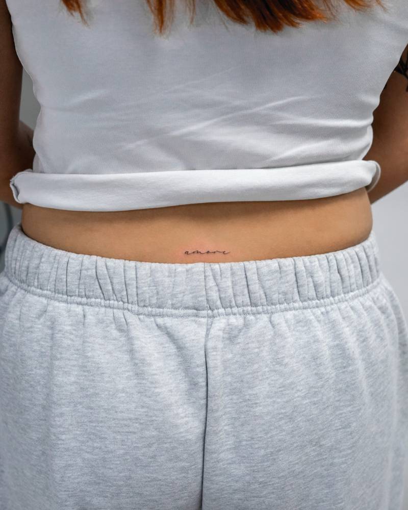 Handwritten font word "amore" tattooed on the lower back.