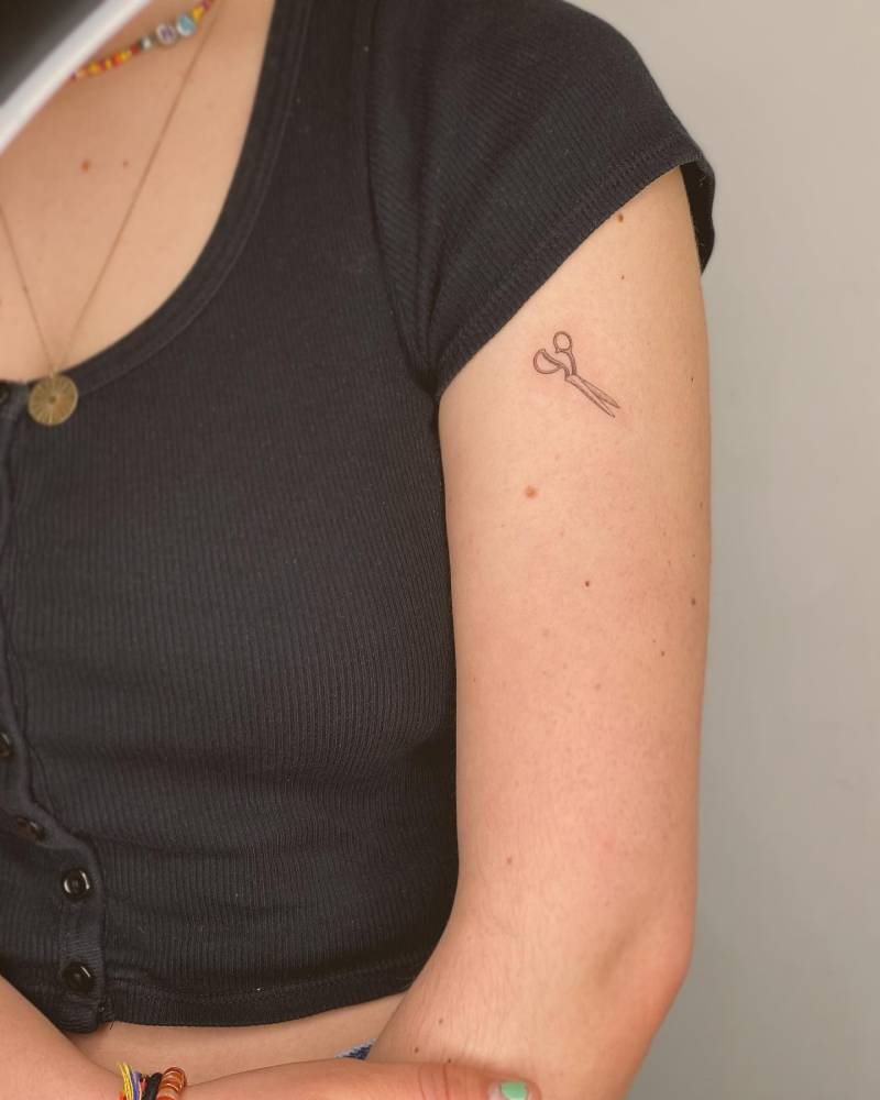 Little scissors tattoo in fine line style placed on the upper arm.