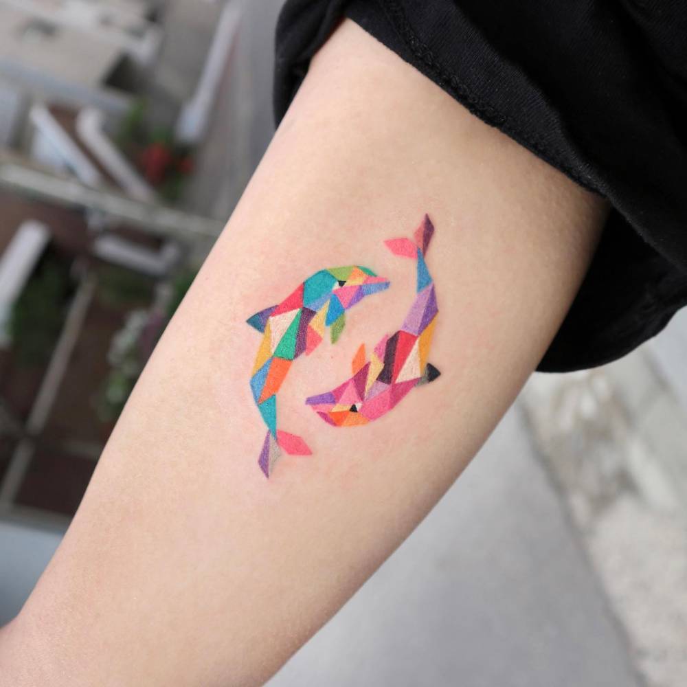 Little dolphins tattooed on the inner arm, geometric style.