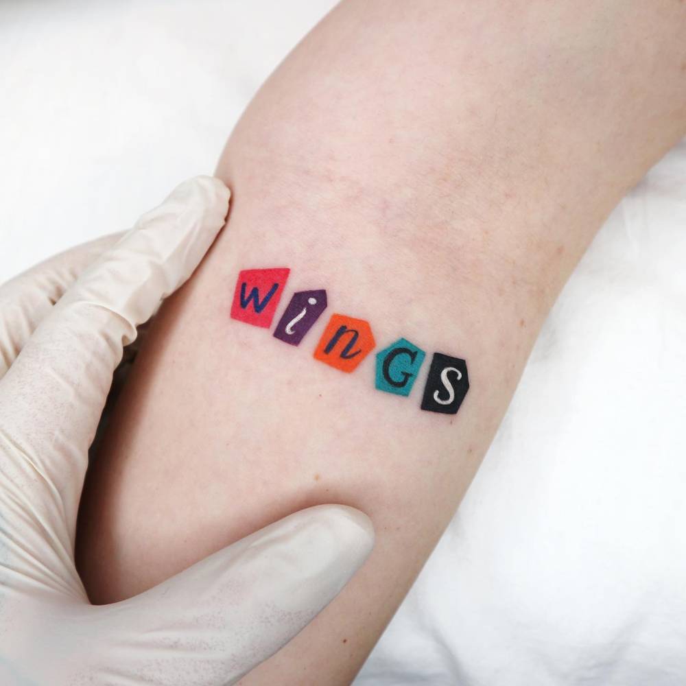 Collage style word "wings" tattoo located on the inner forearm.