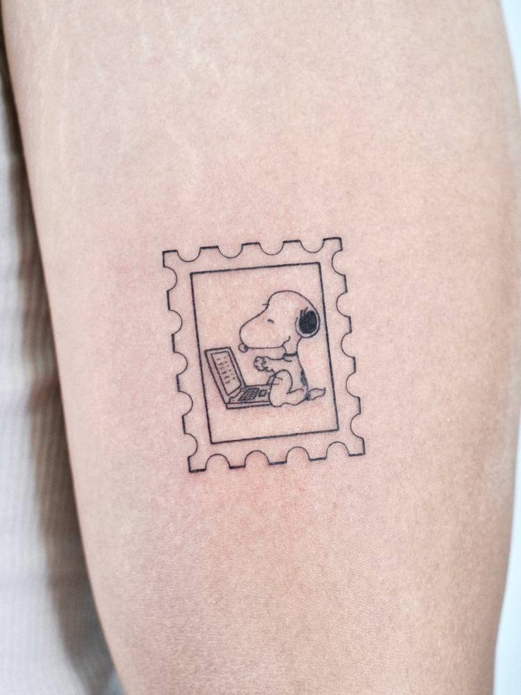 Snoopy stamp tattoo in cartoon style located on the upper arm.
