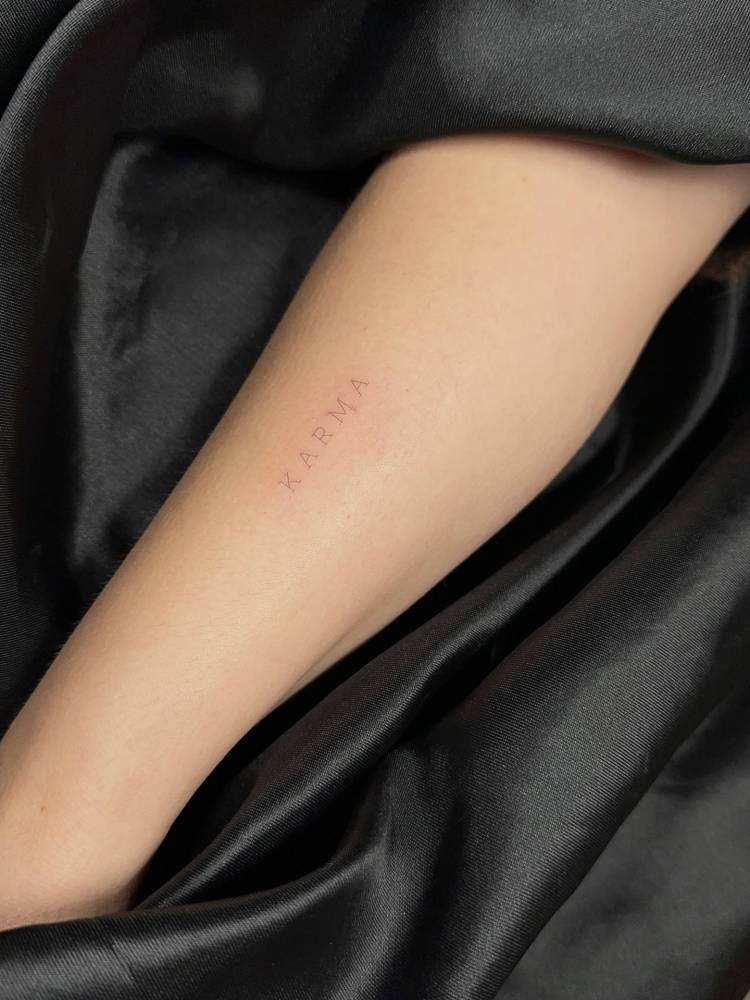 Typewriter font word "karma" tattoo located on the forearm.