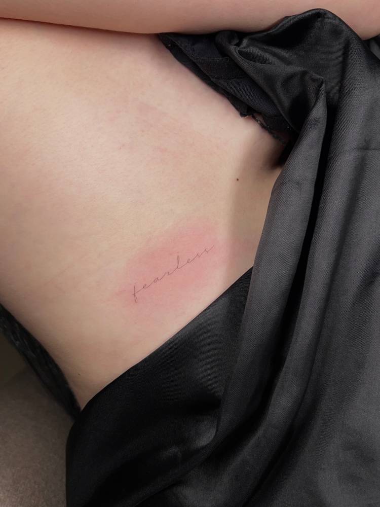 Word "fearless" lettering tattoo handwritten on the rib.
