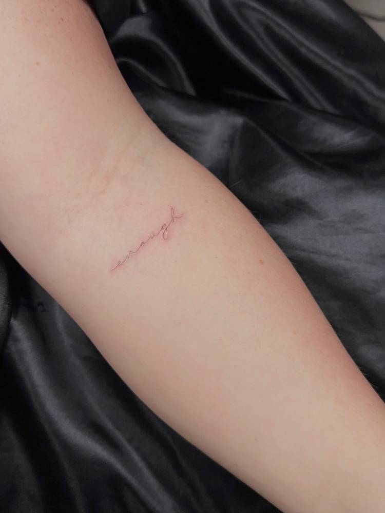 Lettering tattoo of the word "enough" located on the inner forearm.