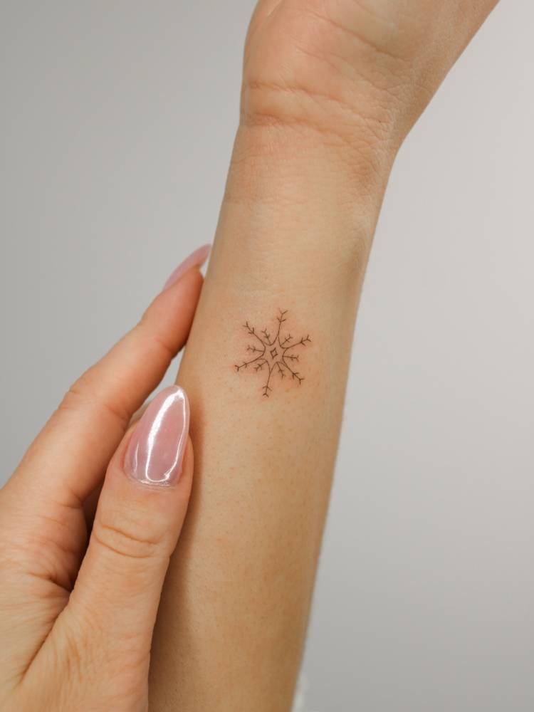 Tiny snowflake tattoo in fine line style done on the wrist.