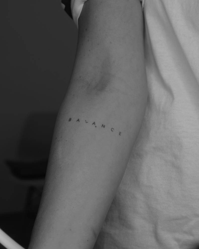 Tattoo of the word "balance" located on the inner forearm.