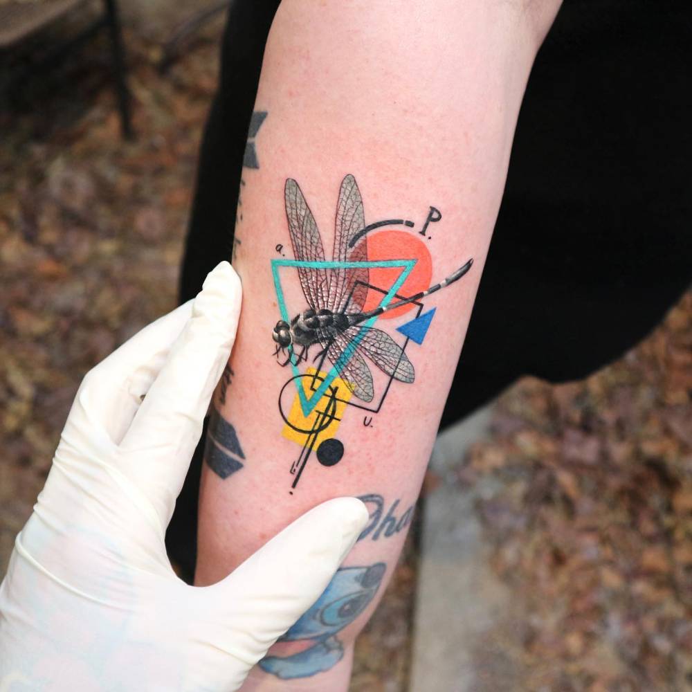Graphic style dragonfly tattoo located on the forearm.