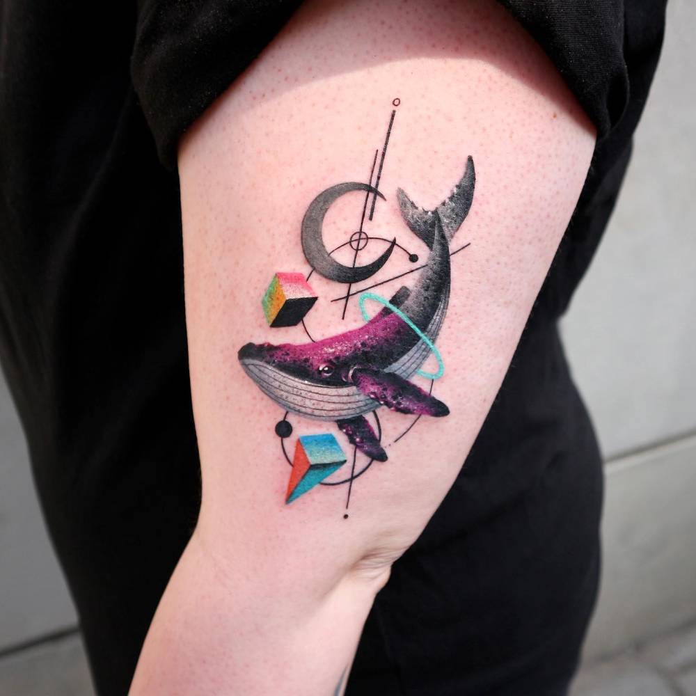 Whale tattoo located on the upper arm, done in graphic style.