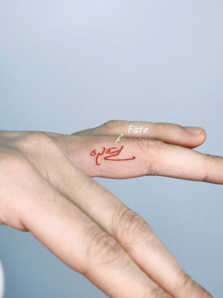 Handwritten font word "fate" in red ink tattooed on the finger.