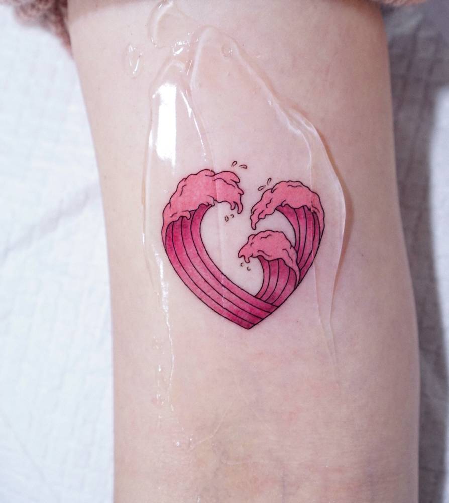 Waves forming a heart tattooed on the bicep, done in illustrative style.