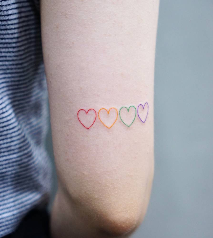 Colorful little hearts tattooed on the tricep, minimalistic style.