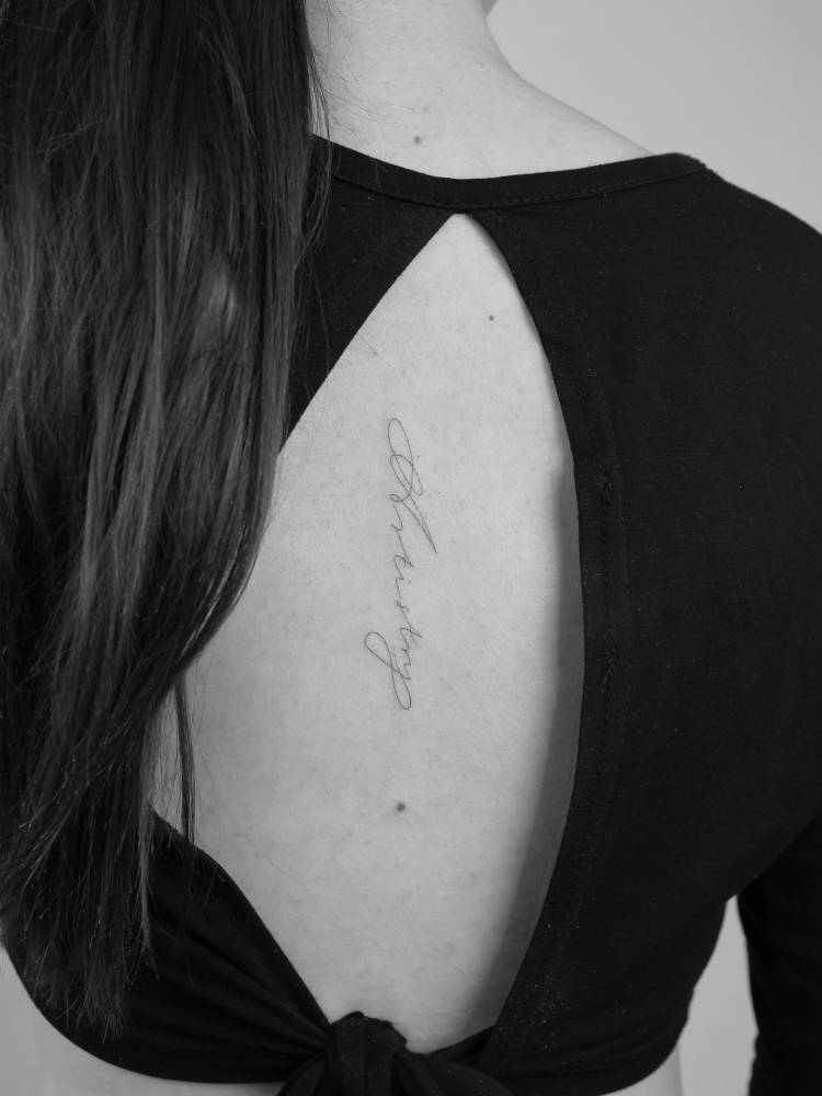 "Artistry" lettering tattoo in handwritten font located on the back.