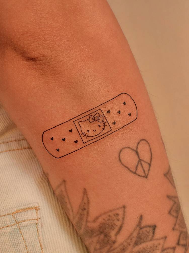 Hello Kitty bandage tattoo located on the forearm, cartoon style.